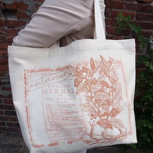 Op de afbeelding: Een witte canvas tote bag met een vintage botanische illustratie van een plant. De illustratie is in roze en bruine tinten. De tekst op de tas luidt "The English Herbal or History of Plants".