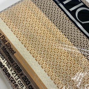 May include: A packaged flat sheet set with a geometric pattern in shades of brown and beige. The set includes a flat sheet for a mattress size of 78 x 80 inches (198 x 203 cm). The packaging is clear plastic.