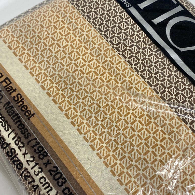 May include: A packaged flat sheet set with a geometric pattern in shades of brown and beige. The set includes a flat sheet for a mattress size of 78 x 80 inches (198 x 203 cm). The packaging is clear plastic.