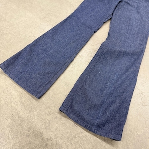 May include: A pair of blue denim bell-bottom trousers. The trousers have a high waist and a wide flare from the knee down. The denim is a medium wash, and the trousers appear to be vintage.