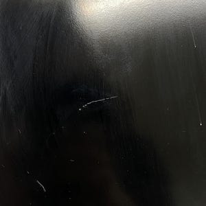 May include: Close-up of a black, glossy surface with visible scratches and imperfections. The surface has a reflective quality, with subtle variations in tone and texture. The image highlights the details of the material.