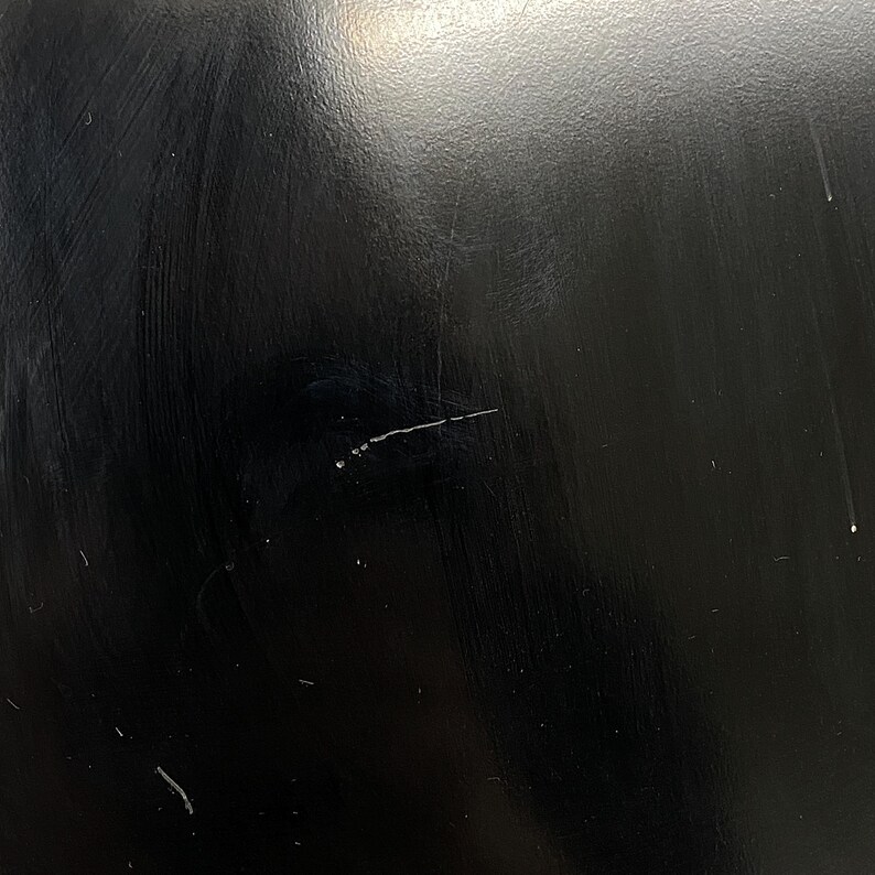 May include: Close-up of a black, glossy surface with visible scratches and imperfections. The surface has a reflective quality, with subtle variations in tone and texture. The image highlights the details of the material.