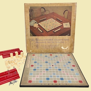 May include: Vintage Scrabble crossword game set. The game includes a board, letter tiles, red tile racks, and the original box. The box features an image of a Scrabble game in progress. The board has colored squares for bonus points.