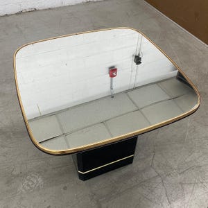 May include: A square coffee table with a mirrored top and a gold-colored trim. The base is black with a gold accent. The table is approximately 30 inches wide and 30 inches long.