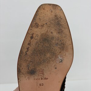 May include: Close-up of a shoe sole with the brand name "VIA SPIGA" embossed. The sole is brown with wear and tear, and the text "MADE IN ITALY" is visible. The size is 52.