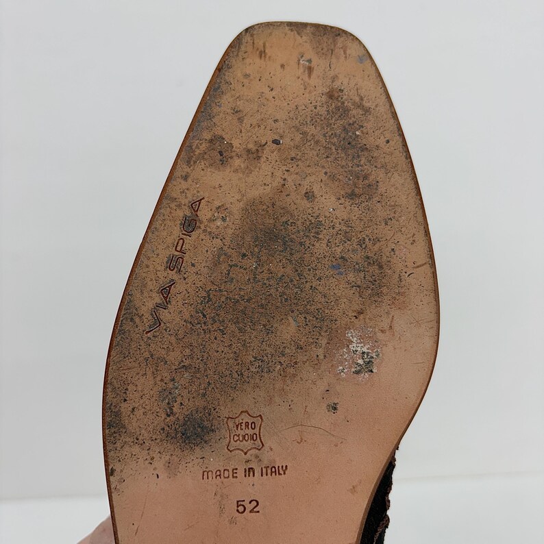 May include: Close-up of a shoe sole with the brand name "VIA SPIGA" embossed. The sole is brown with wear and tear, and the text "MADE IN ITALY" is visible. The size is 52.