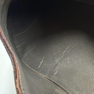 May include: Close-up of the interior of a brown shoe. The shoe's interior is dark brown with visible wear and tear, including cracks and peeling. The edges of the shoe are visible, showing a patterned fabric.