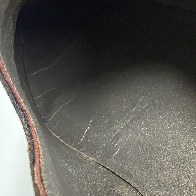 May include: Close-up of the interior of a brown shoe. The shoe's interior is dark brown with visible wear and tear, including cracks and peeling. The edges of the shoe are visible, showing a patterned fabric.