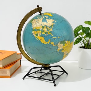 May include: A vintage globe with a teal blue ocean and yellow and green continents. The globe is mounted on a black metal stand and has a brass-colored meridian and axis. The globe is a decorative item.