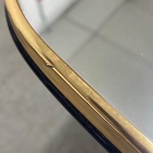 May include: Close-up of a vintage mirror with a gold-colored frame and a dark blue border. The mirror's surface reflects a blurred image. The frame shows signs of wear.