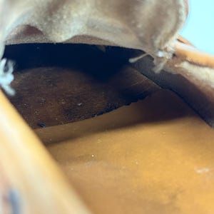 May include: The interior of a tan leather shoe showing a dark brown suede footbed and a smooth tan leather lining. The upper edge of the shoe opening is visible with raw leather edges and visible stitching along the side of the shoe construction.