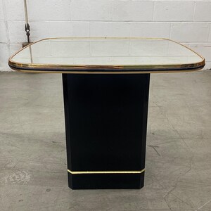 May include: A black side table with a mirrored top and gold trim. The table has a rectangular base and a square top. The table is approximately 24 inches tall and 24 inches wide.