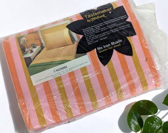 May include: A package of Tastemaker by Mohawk Carousel queen flat sheet in a pink and orange vertical striped pattern. The packaging features a black floral-shaped label with product details and an image of a bed with striped bedding.