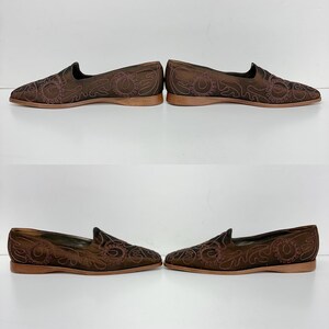 May include: Four pairs of brown slip-on shoes with detailed embroidered floral patterns. The shoes feature a low profile, a rounded toe, and a thin, light brown sole. The embroidery is a darker brown, creating a contrasting design.