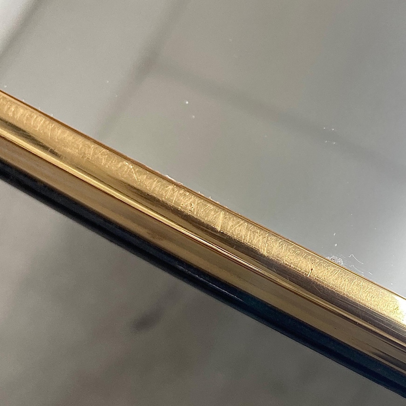 May include: Close-up of a gold-colored metal frame with a dark blue edge. The frame has a brushed texture and appears to be part of a mirror or picture frame. The gold color has a slight sheen, reflecting the light.