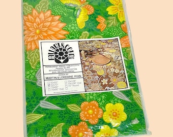 May include: A green tablecloth with a floral pattern in shades of orange, yellow, and green. The tablecloth is packaged in plastic and has a label that reads "Faladi & Co. Inc. Permanent Press Tablecloth Paradise No. 769 50% Polyester 50% Cotton Soil Release Finish Design by Martin & Lorraine Ryan" and lists various sizes.
