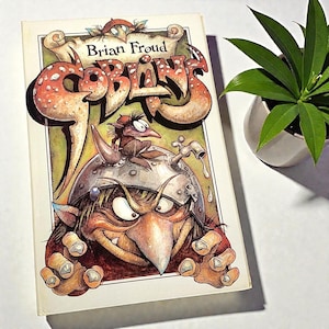 May include: A hardcover book titled "Goblins" by Brian Froud. The cover features a detailed illustration of a goblin with a large nose, wearing a helmet with a faucet, and a small goblin on top. The title is in large, stylized letters.