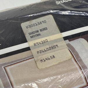 May include: A package of Shadow Boxes Neutral, with a product label. The label includes the text "SHADOW BOXES NEUTRAL" and several numerical codes. The packaging is clear plastic, and the product appears to have a beige and brown pattern.
