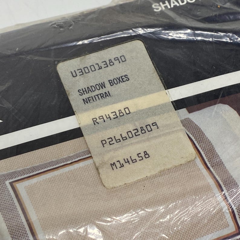 May include: A package of Shadow Boxes Neutral, with a product label. The label includes the text "SHADOW BOXES NEUTRAL" and several numerical codes. The packaging is clear plastic, and the product appears to have a beige and brown pattern.