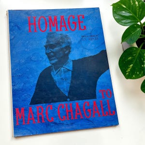May include: A vintage magazine cover with a blue background and the words "HOMAGE TO MARC CHAGALL" in red. The cover features a portrait of a man in a dark jacket and a light blue shirt. The text "SPECIAL ISSUE OF XX SIECLE" is also visible.