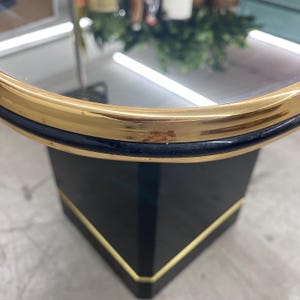 May include: A round, black and gold accent table with a mirrored top. The table has a gold trim around the top and base, and a black base with gold accents. The table is a modern design.
