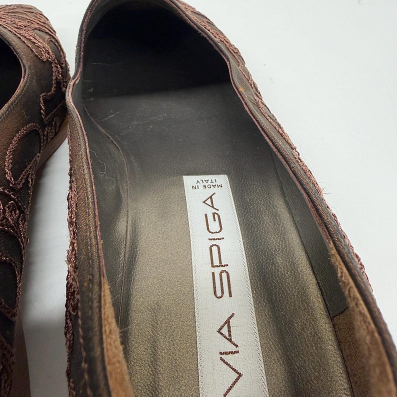 May include: Close-up of a brown Via Spiga shoe. The shoe has a textured design on the upper and a dark brown interior. The label inside the shoe reads "MADE IN ITALY".