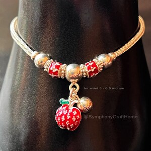 May include: Silver bracelet with red enamel charms and a dangling red apple charm with a green stem and a silver bell. The bracelet is for a wrist size of 5 to 6.5 inches. @SymphonyCraftHome