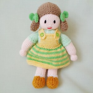 May include: A knitted doll with brown hair, green bows, a yellow and green striped dress, and yellow shoes.
