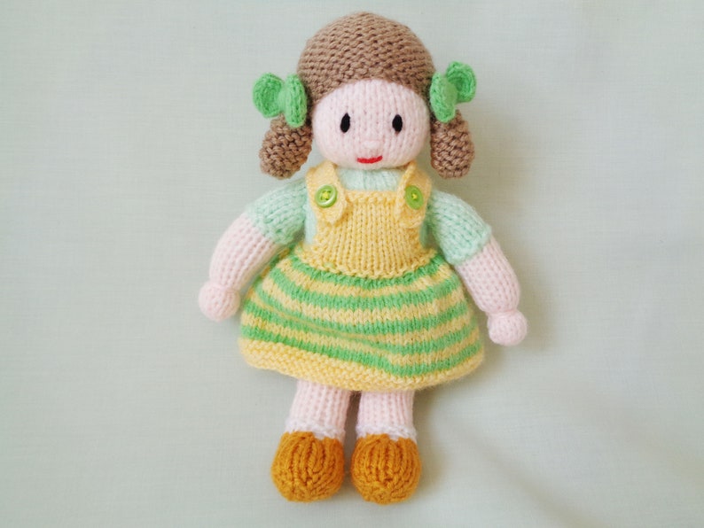 May include: A knitted doll with brown hair, green bows, a yellow and green striped dress, and yellow shoes.