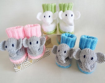 May include: Three pairs of knitted baby booties with elephant faces. The booties are in pink, blue, and green.