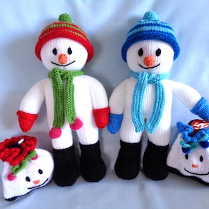 Puede incluir: Dos muñecos de nieve tejidos con cuerpos blancos, botas negras y narices de zanahoria naranjas. Un muñeco de nieve lleva un gorro rojo y verde, una bufanda verde y manoplas rojas. El otro lleva un gorro azul, bufanda y manoplas.