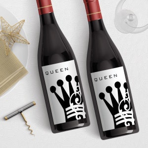 Puede incluir: Dos botellas de vino tinto con etiquetas en blanco y negro. Las etiquetas presentan la palabra "QUEEN" y un diseño de corona estilizado.