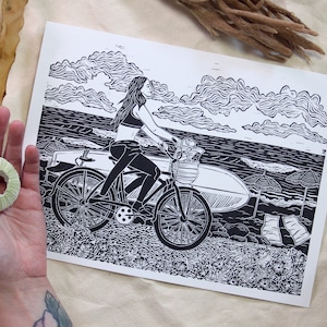 Lovely Day - hand-printed lino-cut block print - depicting a surfer biking to the beach - ocean, surf, swim, bicycle, outdoors, nature