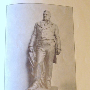 May include: Black and white photograph of a statue of John Middleton Clayton. The statue depicts Clayton standing with his right hand on his hip and his left hand holding a book. The statue is on a pedestal. The text below the image reads "JOHN MIDDLETON CLAYTON JULY 24, 1796 - NOVEMBER 9, 1856".