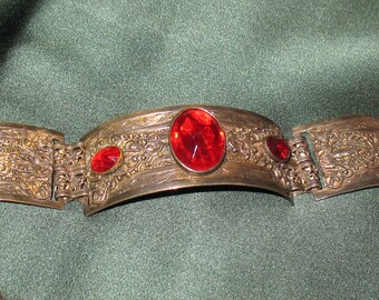 May include: A silver bracelet with an ornate design and three red glass stones.