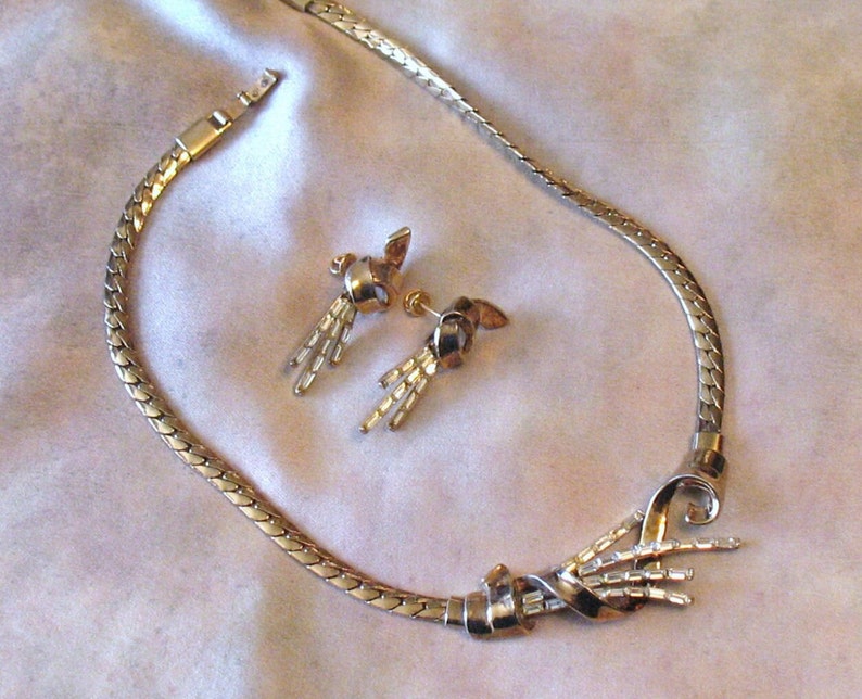 May include: A gold-tone necklace with a twisted design and matching earrings. The necklace has a chain link style and the earrings have a dangling design.