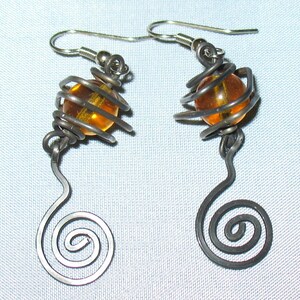 May include: A pair of silver earrings with a spiral design and an amber glass bead encased in a wire cage.