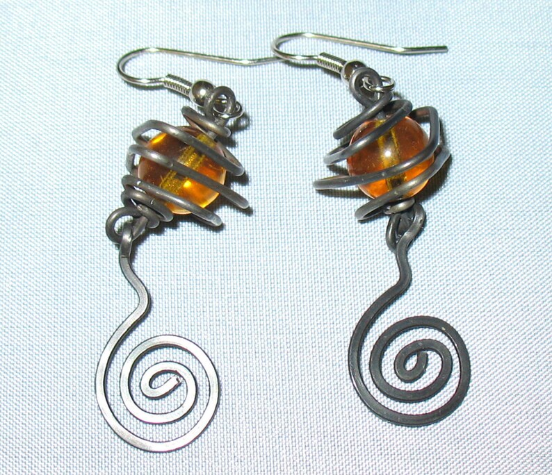 May include: A pair of silver earrings with a spiral design and an amber glass bead encased in a wire cage.