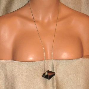 Puede incluir: Un collar de cadena de plata con un colgante de cuero marr&oacute;n. El colgante tiene forma de cono y tiene una peque&ntilde;a perla en el centro.