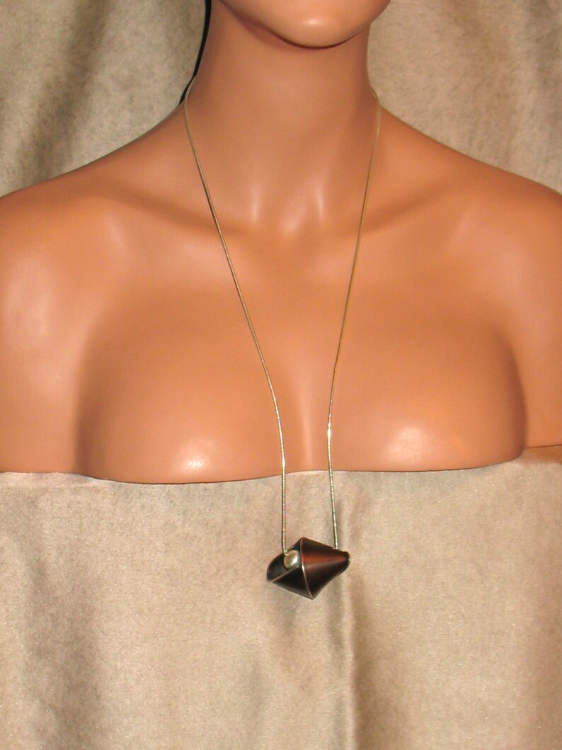 Puede incluir: Un collar de cadena de plata con un colgante de cuero marr&oacute;n. El colgante tiene forma de cono y tiene una peque&ntilde;a perla en el centro.