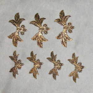 May include: Set of eight gold-toned metal leaf-shaped embellishments. Each embellishment features a central design of three small circles and a raised, textured leaf pattern.