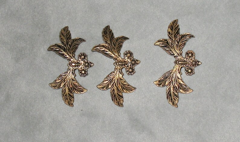 May include: Three gold-colored metal leaf-shaped embellishments with a textured surface.
