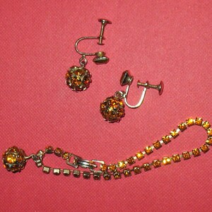 May include: A set of amber rhinestone jewelry including a pair of clip-on earrings and a necklace.