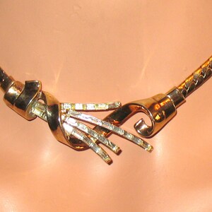 May include: A gold-toned necklace with a twisted design and clear rhinestones. The necklace is made of a chain link style.
