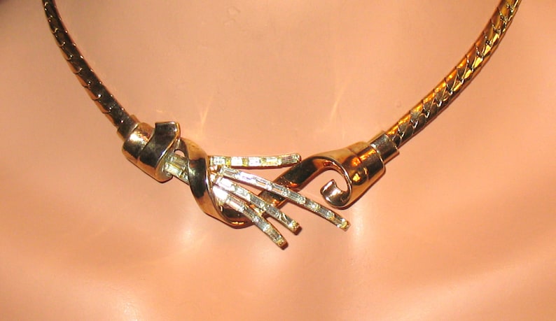 May include: A gold-toned necklace with a twisted design and clear rhinestones. The necklace is made of a chain link style.