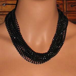 May include: A black beaded necklace with multiple strands of faceted beads. The necklace is layered and creates a thick, dramatic look.