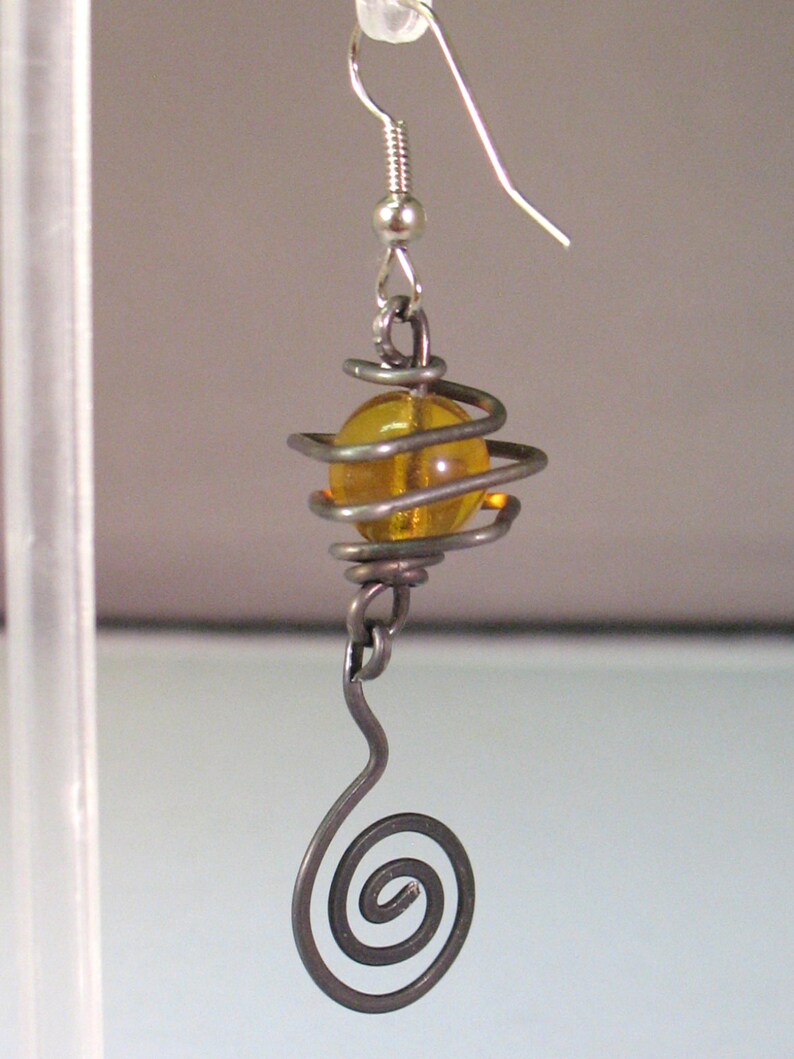 May include: A silver wire earring with a spiral design and an amber glass bead.