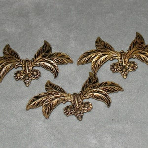 May include: Three gold-toned metal decorative embellishments shaped like stylized leaves with a floral design in the center.