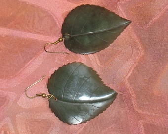 May include: A pair of leaf-shaped earrings made of dark green jade. The earrings are suspended from gold-toned hooks.