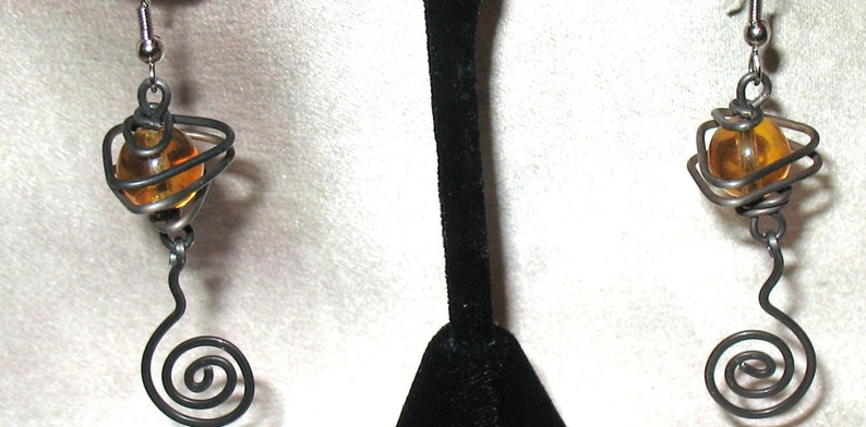 May include: A pair of earrings with a spiral design and a small amber glass bead in the center of each earring.
